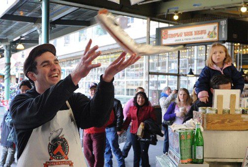 Workers at Pike Place Fish Market in Seattle throwing fish and engaging with customers, showing a fun workplace culture built on an attitude of gratitude.