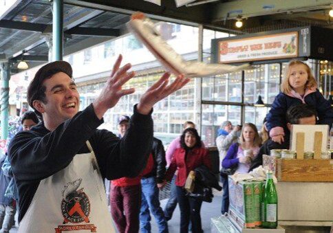 Workers at Pike Place Fish Market in Seattle throwing fish and engaging with customers, showing a fun workplace culture built on an attitude of gratitude.